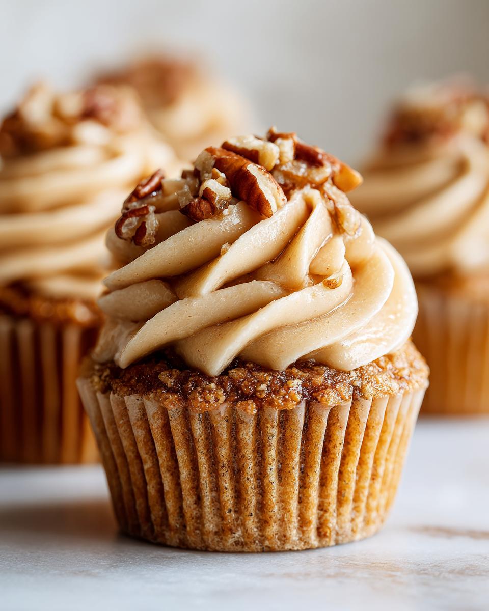 A close-up of a single pecan pie cupcake topped with swirled brown frosting and chopped pecans.