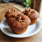 Three freshly baked morning glory muffins, topped with pecans, resting on a small white plate.