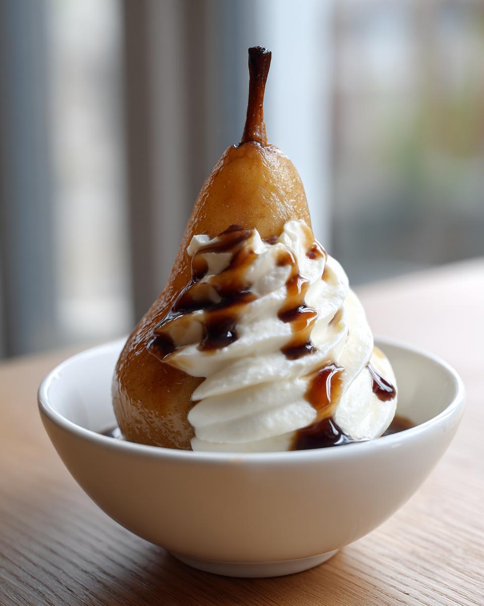 A single poached pear topped with a swirl of whipped cream and drizzled with dark syrup, served in a white bowl.