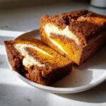 Two slices of moist pumpkin cream cheese bread showing a beautiful cream cheese swirl, served on a white plate.