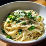 Close-up of creamy spaghetti tossed in a light sauce, topped generously with grated parmesan pasta and fresh chopped parsley.