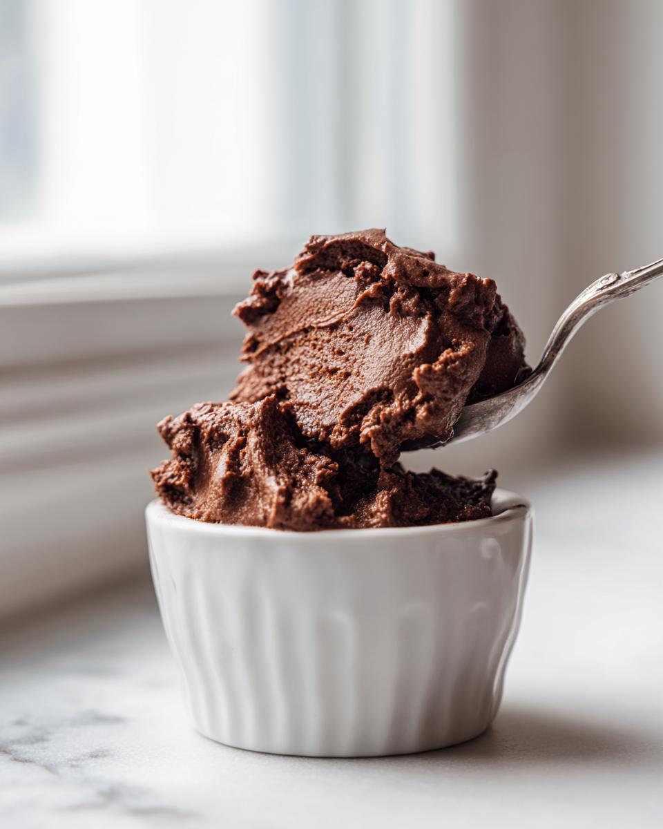 A spoonful of rich, dark chocolate mousse being lifted from a small white ramekin.