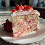 A tall slice of light sponge strawberry cake layered with pink cream and topped with whipped cream and fresh strawberries.