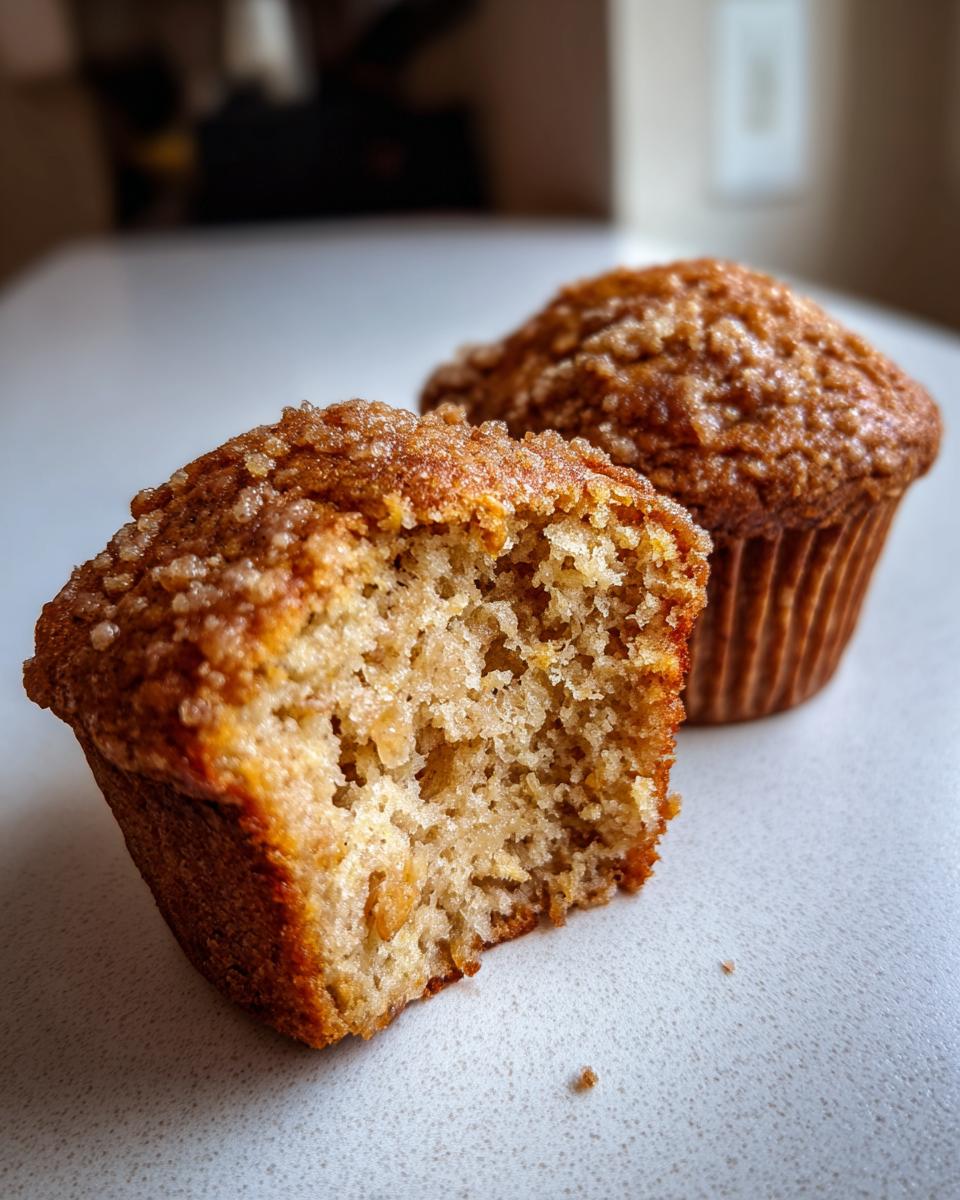 Close-up of a sourdough discard banana muffin cut in half showing the moist interior and a second whole muffin behind it.
