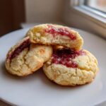 A stack of three strawberry cheesecake cookies, one cut in half showing the creamy filling and strawberry jam topping.