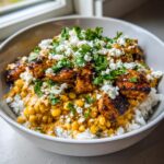 A close-up of a vibrant street corn chicken rice bowl featuring seasoned chicken, creamy corn sauce, white rice, cotija cheese, and fresh cilantro.