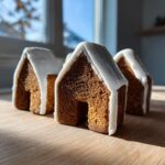 Three small, baked gingerbread house pieces decorated with white royal icing roofs, ready for assembly using this gingerbread house recipe.