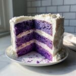 Cross-section view of a multi-layered lavender cake with bright purple layers and white frosting.