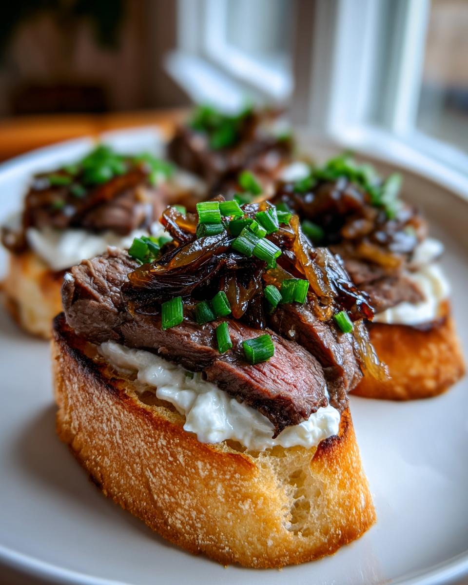Close-up of a gourmet steak crostini topped with creamy cheese, sliced steak, caramelized onions, and chives.