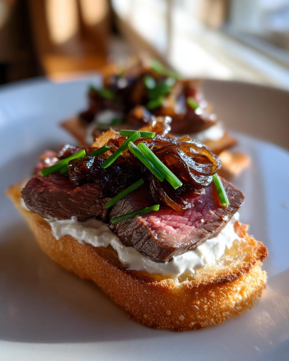 Close-up of a perfectly cooked steak crostini topped with creamy cheese, caramelized onions, and fresh chives.